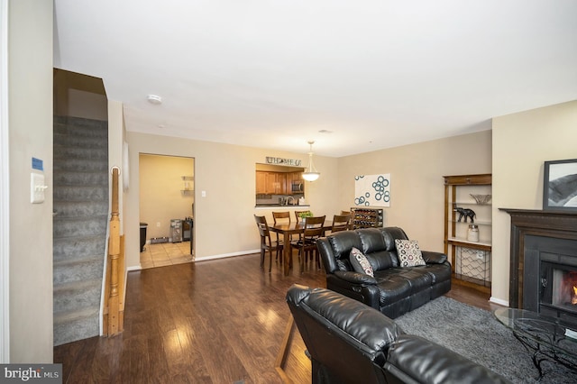 living room featuring stairs, a lit fireplace, wood finished floors, and baseboards