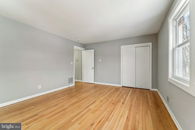 unfurnished bedroom with a closet, light hardwood / wood-style floors, and multiple windows