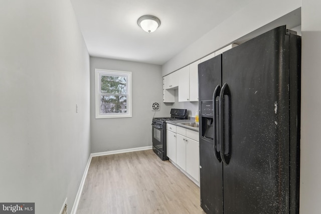 kitchen featuring white cabinetry, light hardwood / wood-style floors, and black appliances