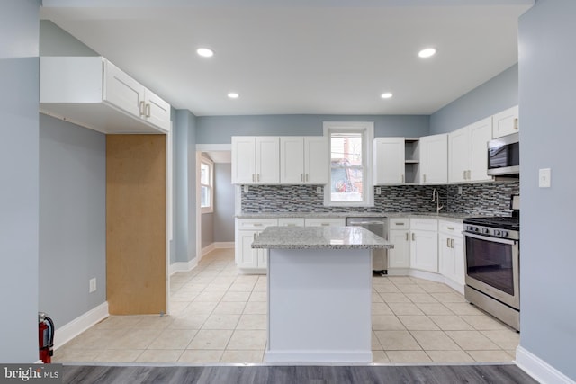 kitchen featuring appliances with stainless steel finishes, white cabinetry, a center island, light stone countertops, and decorative backsplash