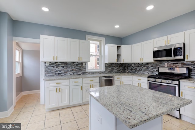 kitchen with white cabinetry, light stone countertops, stainless steel appliances, and a center island