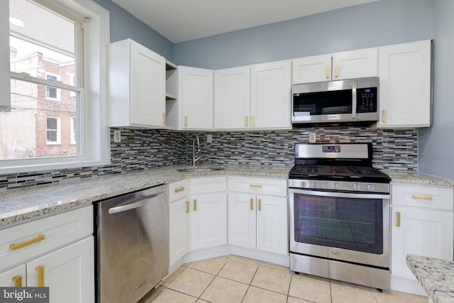 kitchen with appliances with stainless steel finishes, sink, white cabinets, decorative backsplash, and light stone countertops