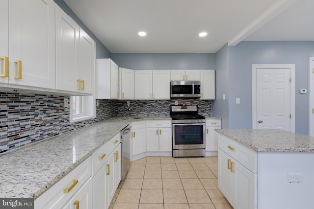 kitchen featuring appliances with stainless steel finishes, light stone counters, white cabinets, light tile patterned flooring, and decorative backsplash