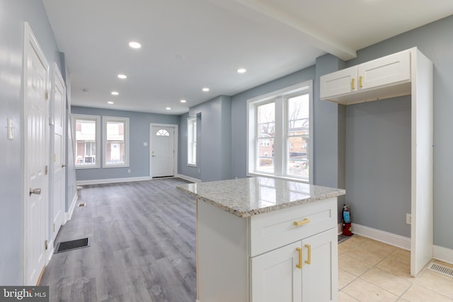 kitchen featuring light hardwood / wood-style flooring, white cabinetry, light stone countertops, a kitchen island, and beamed ceiling