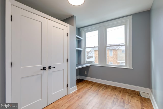 unfurnished bedroom featuring built in desk, light hardwood / wood-style floors, and a closet