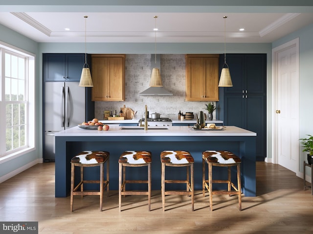 kitchen with pendant lighting, sink, stainless steel refrigerator, a kitchen island with sink, and wall chimney exhaust hood