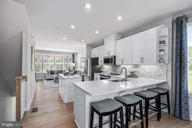 kitchen featuring a breakfast bar, sink, white cabinetry, appliances with stainless steel finishes, and kitchen peninsula