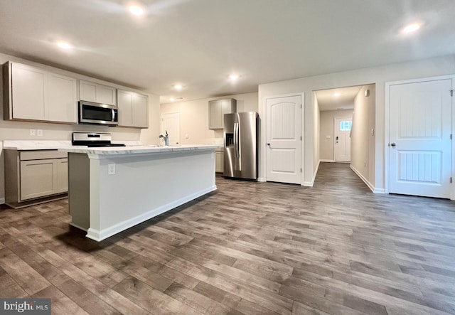 kitchen with sink, gray cabinetry, stainless steel appliances, dark wood-type flooring, and a center island with sink