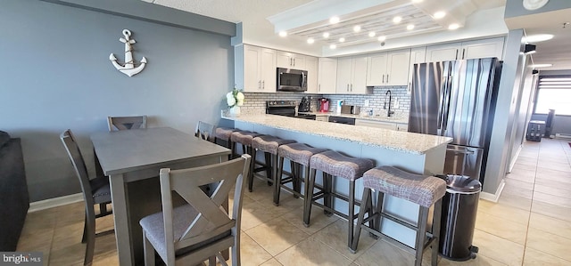 kitchen featuring sink, light tile patterned floors, appliances with stainless steel finishes, backsplash, and a kitchen breakfast bar