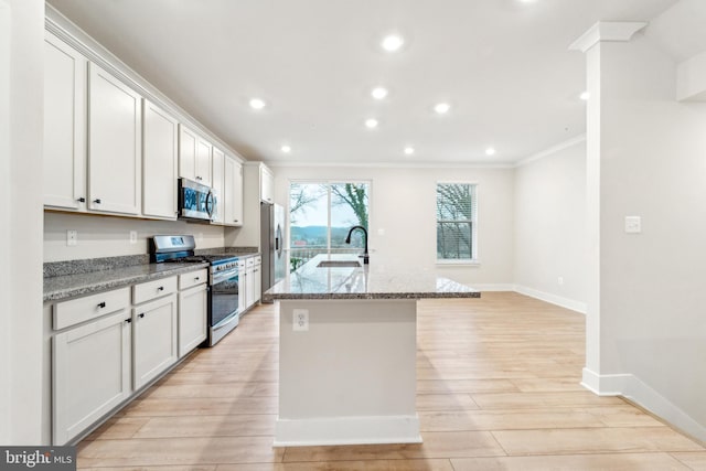 kitchen featuring appliances with stainless steel finishes, ornamental molding, a sink, an island with sink, and light wood-type flooring