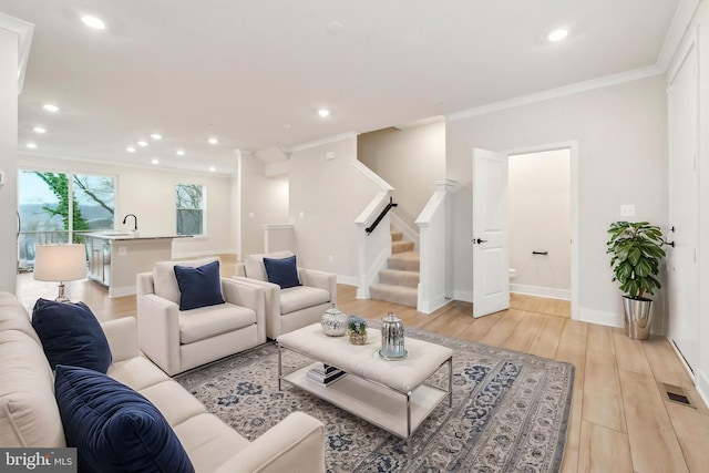 living area featuring light wood finished floors, recessed lighting, visible vents, stairway, and ornamental molding