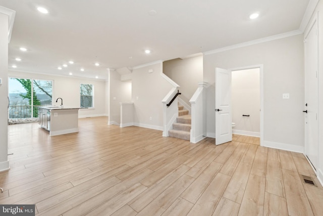 unfurnished living room featuring visible vents, light wood-style flooring, ornamental molding, stairs, and a sink