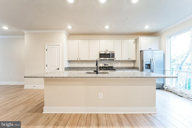 kitchen featuring stainless steel appliances, a sink, ornamental molding, and an island with sink