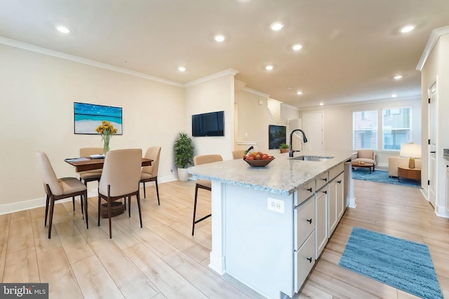 kitchen featuring a center island with sink, light stone counters, light wood-type flooring, white cabinetry, and a sink