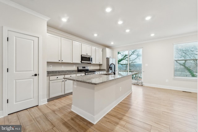 kitchen featuring stainless steel appliances, light wood-style floors, a kitchen island with sink, and ornamental molding