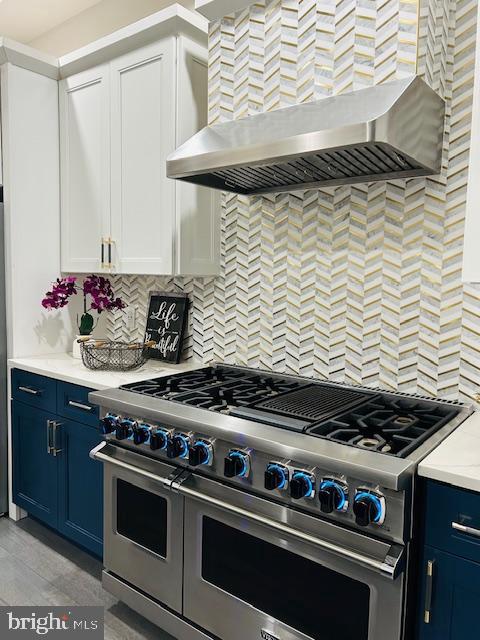 kitchen with white cabinetry, wall chimney exhaust hood, blue cabinets, and range with two ovens