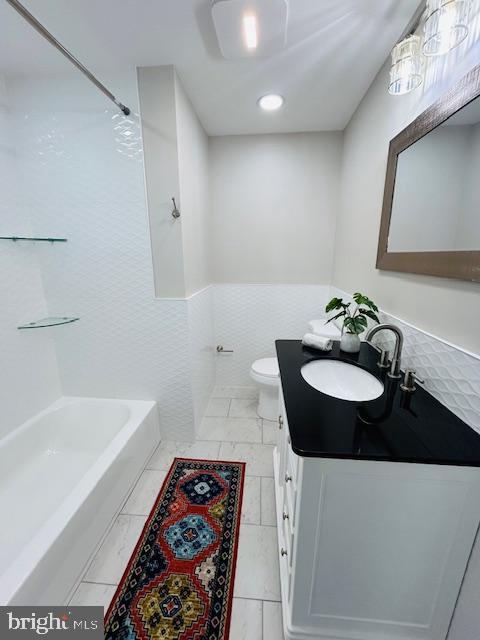 full bathroom featuring vanity, toilet, tub / shower combination, and tile walls