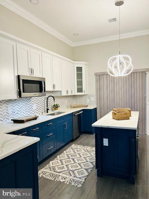 kitchen with blue cabinetry, white cabinetry, appliances with stainless steel finishes, a kitchen island, and pendant lighting