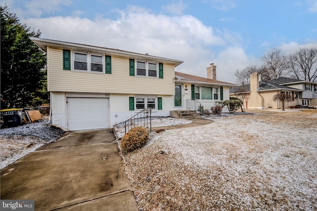 split level home featuring a garage, concrete driveway, and a chimney