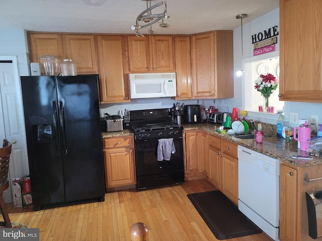 kitchen with hanging light fixtures, light wood-style floors, a sink, dark stone countertops, and black appliances