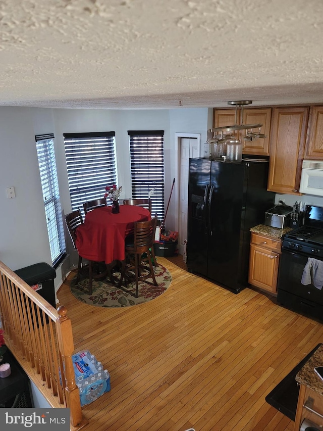 kitchen featuring brown cabinetry, light wood-style floors, a textured ceiling, and black appliances