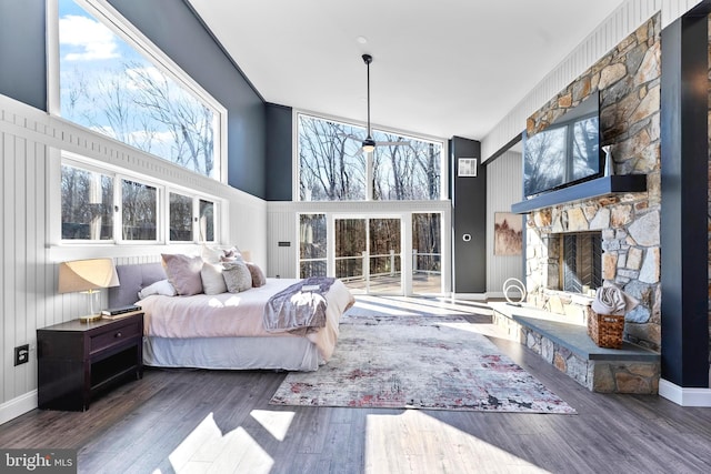 bedroom with baseboards, a fireplace, a high ceiling, and wood finished floors