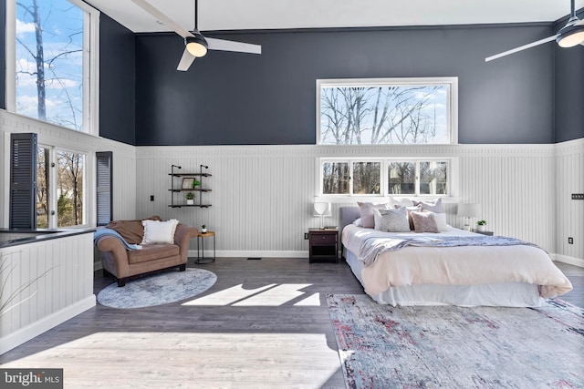 bedroom with a towering ceiling, wainscoting, wood finished floors, and a ceiling fan