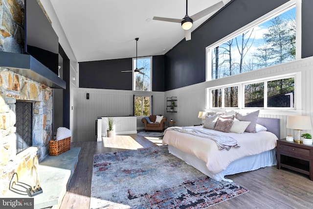 bedroom featuring a stone fireplace, a high ceiling, and wood finished floors