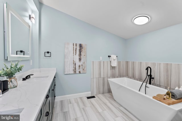 full bathroom with a freestanding bath, vanity, and baseboards