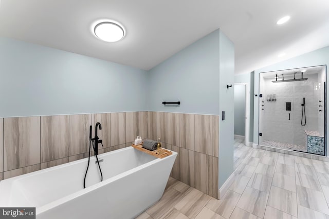 bathroom featuring vaulted ceiling, wainscoting, a stall shower, and a soaking tub