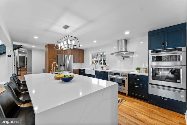 kitchen with light wood-style flooring, recessed lighting, stainless steel appliances, wall chimney range hood, and a warming drawer