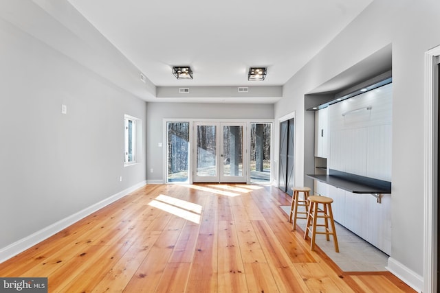 unfurnished living room with light wood finished floors, french doors, visible vents, and baseboards