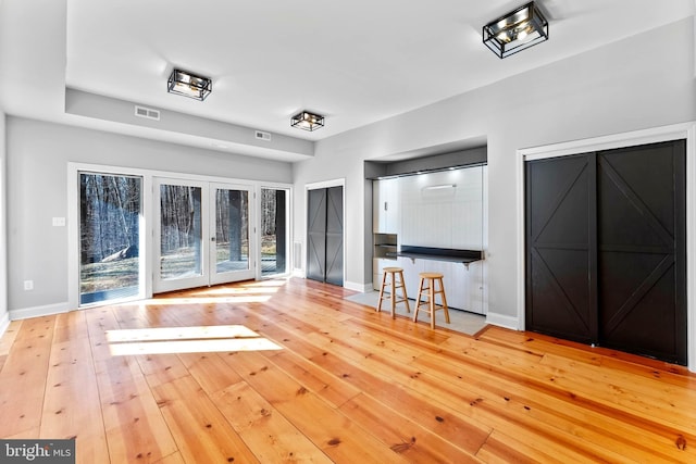 unfurnished living room featuring wood-type flooring, visible vents, and baseboards