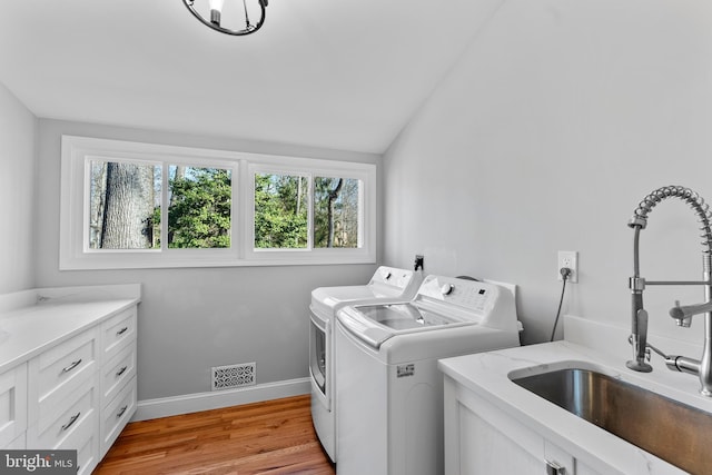 washroom featuring light wood finished floors, cabinet space, visible vents, washing machine and dryer, and a sink