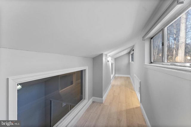 hall featuring lofted ceiling, light wood-style flooring, and baseboards