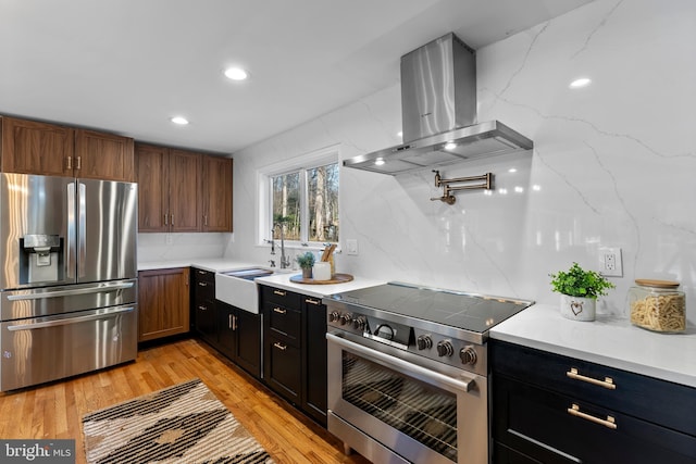 kitchen with stainless steel appliances, backsplash, a sink, ventilation hood, and light wood-type flooring