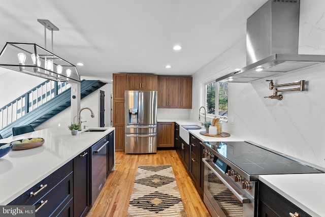 kitchen with light wood-type flooring, appliances with stainless steel finishes, island range hood, and a sink