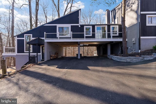 exterior space featuring aphalt driveway, a chimney, and a carport