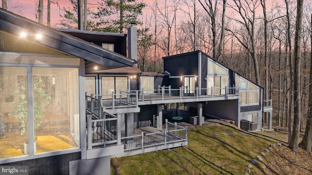 back of property at dusk featuring a patio, cooling unit, a sunroom, a lawn, and a chimney