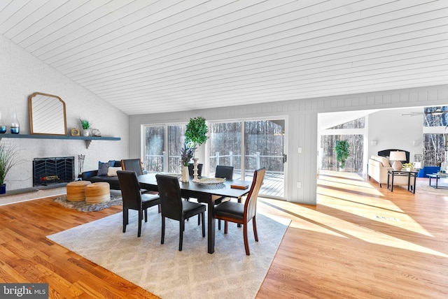 dining area with a warm lit fireplace, vaulted ceiling, and light wood-style flooring