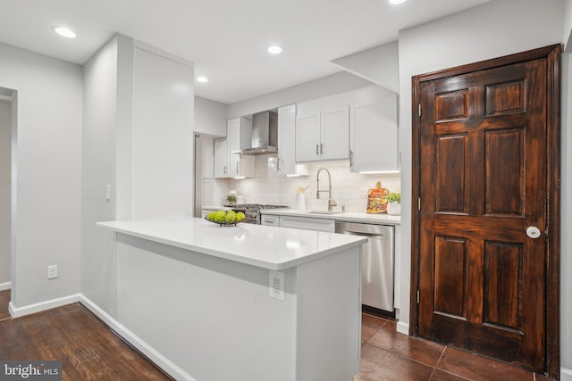 kitchen featuring kitchen peninsula, appliances with stainless steel finishes, wall chimney exhaust hood, white cabinetry, and sink