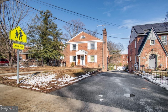 view of front facade with a chimney, fence, and brick siding