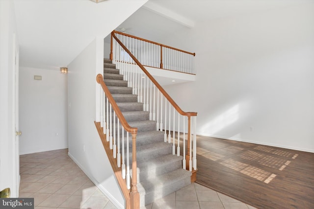 stairway with baseboards, beam ceiling, high vaulted ceiling, and tile patterned flooring