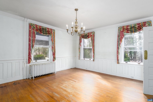 empty room with radiator, a wainscoted wall, a notable chandelier, and wood finished floors