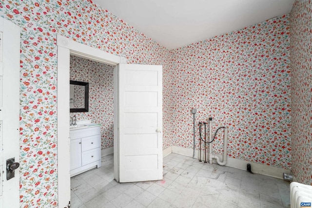 bedroom featuring wallpapered walls, baseboards, light floors, and a sink