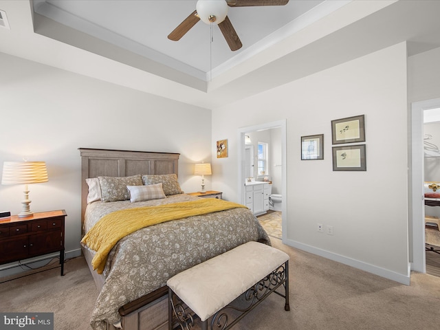 bedroom with ceiling fan, light carpet, ensuite bath, and a tray ceiling