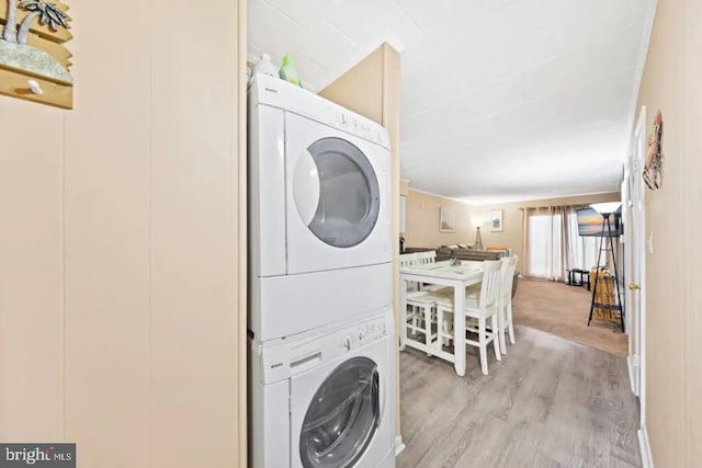 clothes washing area featuring laundry area, light wood-style flooring, and stacked washer and clothes dryer