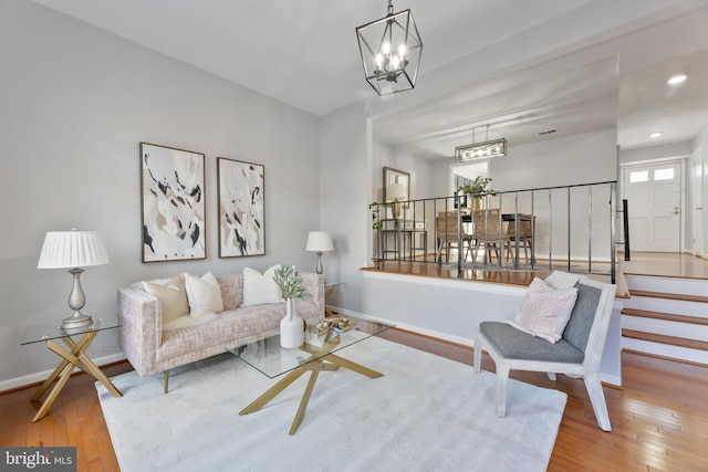 living area with stairway, baseboards, an inviting chandelier, and hardwood / wood-style floors