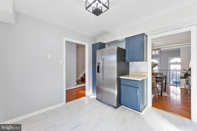 kitchen with light countertops, blue cabinetry, baseboards, and stainless steel refrigerator with ice dispenser