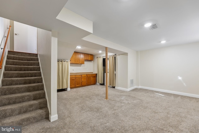 finished basement featuring visible vents, baseboards, light colored carpet, and stairs